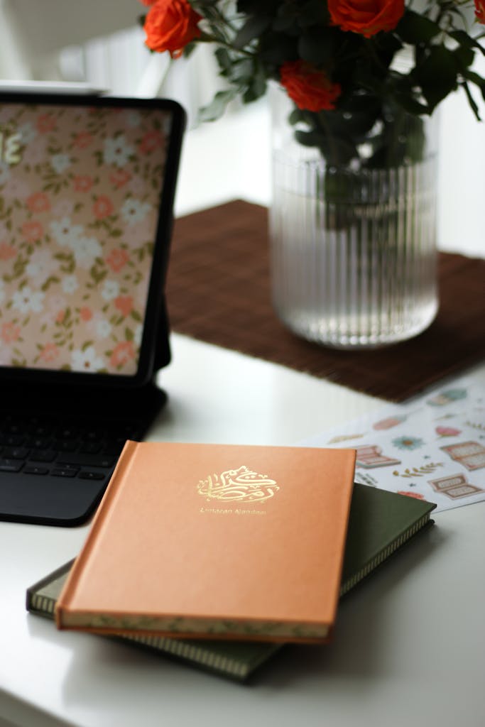 A cozy and stylish workspace featuring a tablet, notebooks, and a vase of red roses.