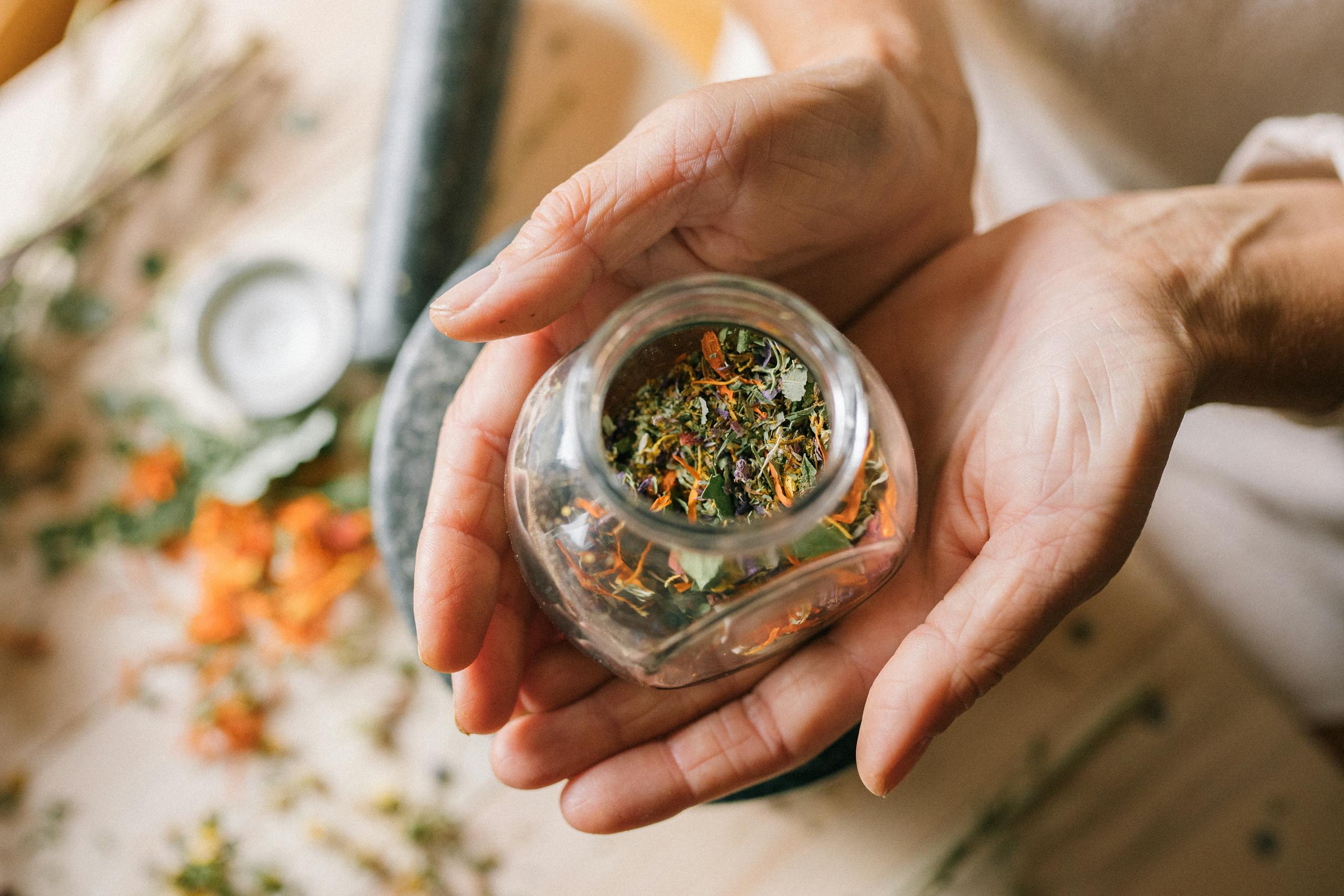 Close-up of hands holding a glass jar filled with colorful dried herbs.